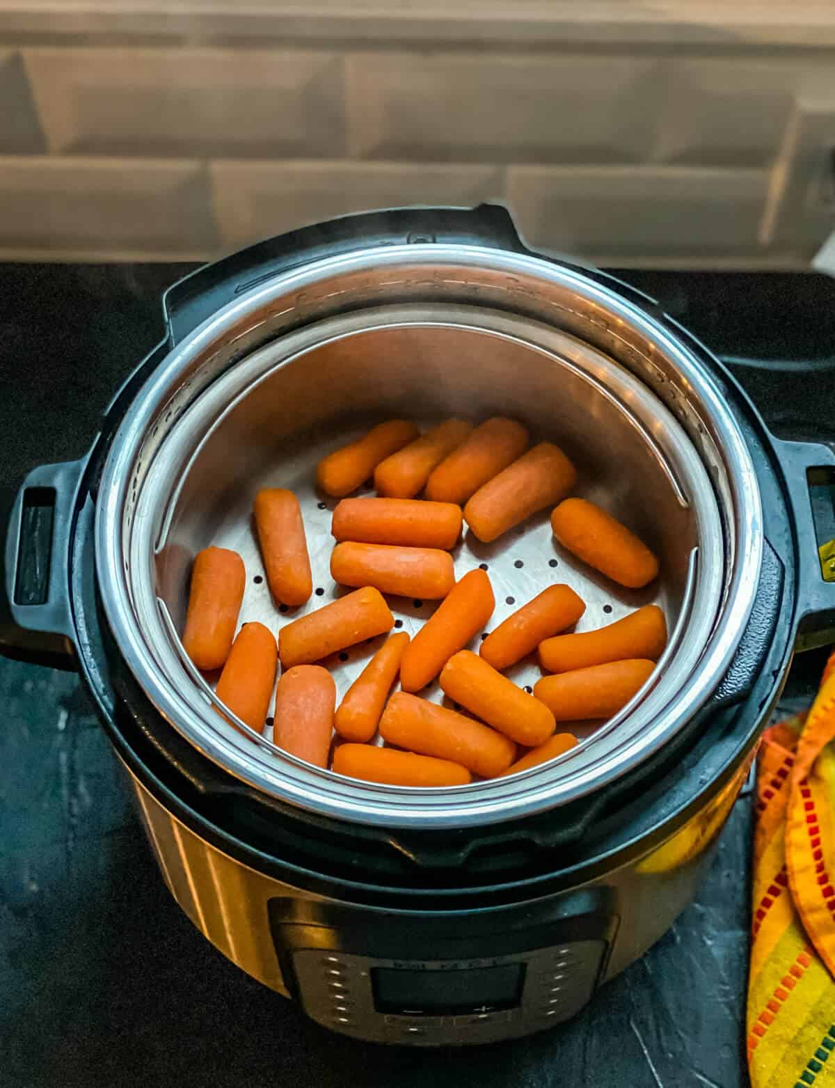 An instant pot with a steamer basket topped with steamed carrots.