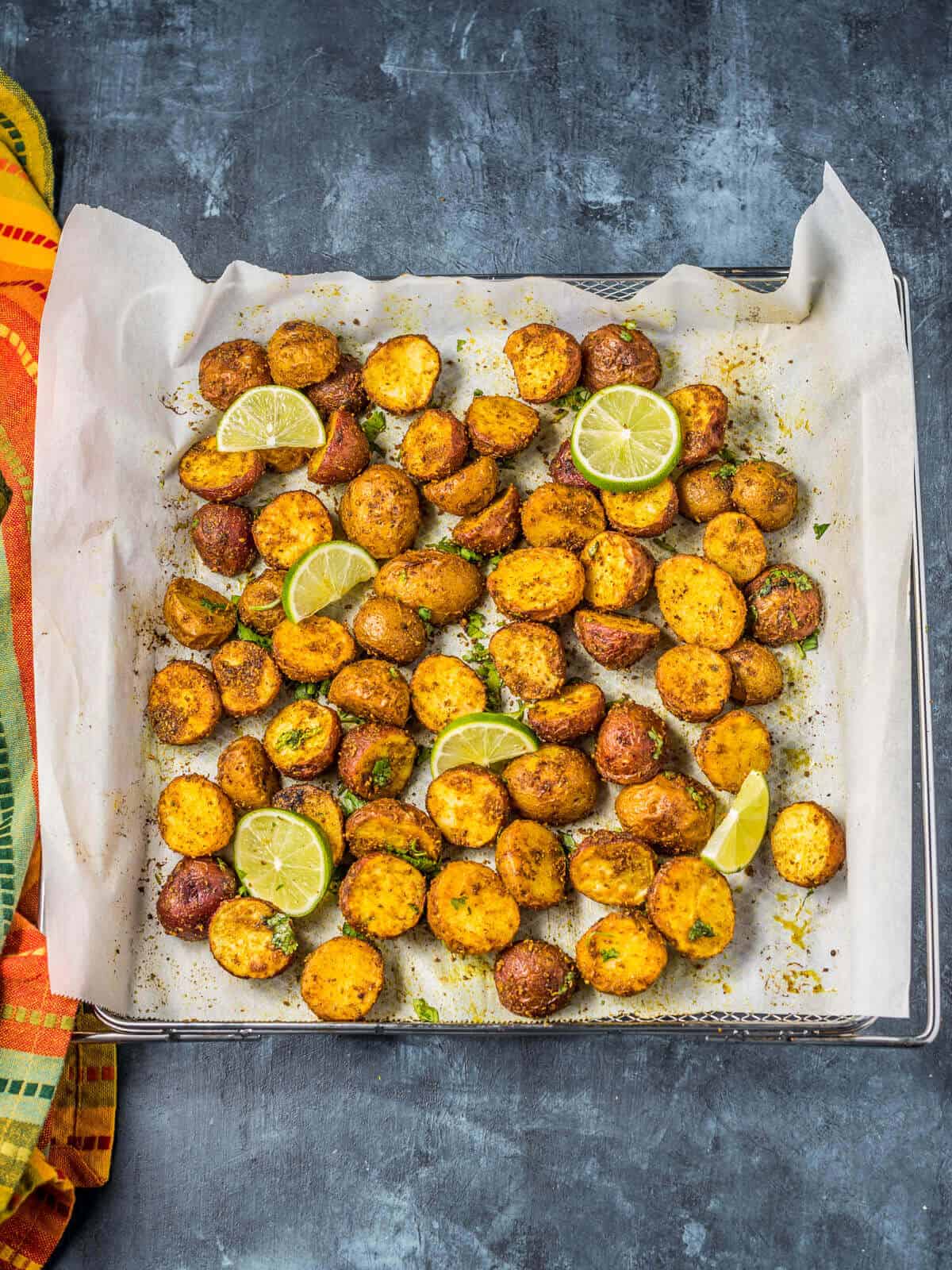 An air fryer tray lined with parchment paper and filled with halved baby potatoes.