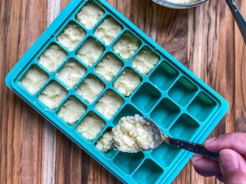 Filling a silicone ice cub tray with minced garlic.
