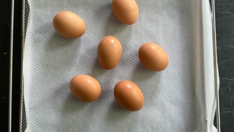 Six eggs on a parchment paper lined air fryer sheet.