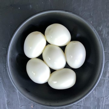 A bowl with six peeled air fryer hard boiled eggs on a grey counter.