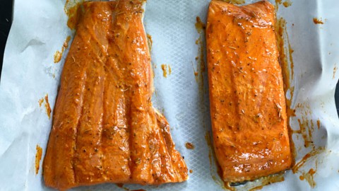 Salmon fillets on a sheet of parchment, brushed with marinade.