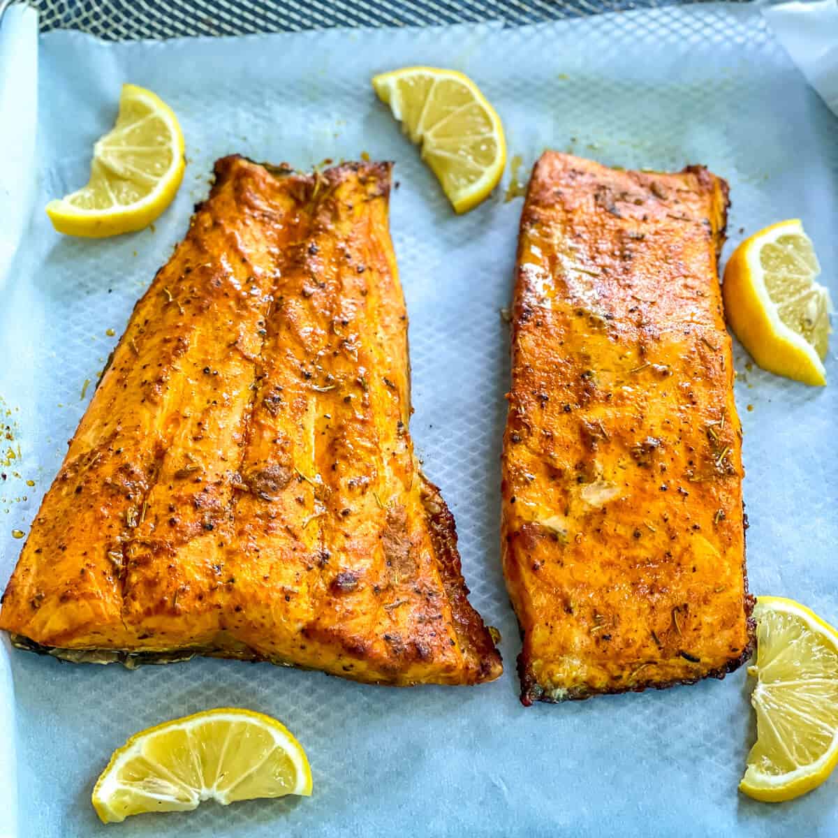 Two pieces of cooked and seasoned salmon, garnished with citrus.