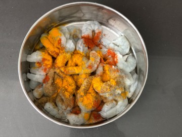 A bowl of raw shrimp with seasoning added.