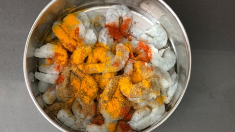 A bowl of raw shrimp with seasoning added.
