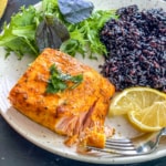 A small portion of salmon, served with black rice and salad.