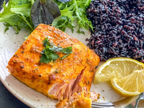 A small portion of salmon, served with black rice and salad.