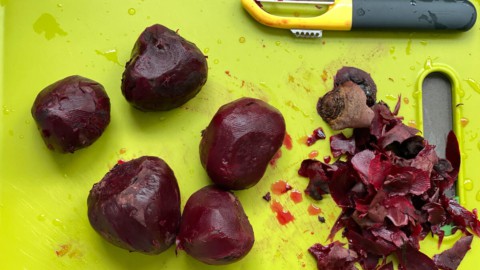 A cutting board with a peeler and peeled beets.