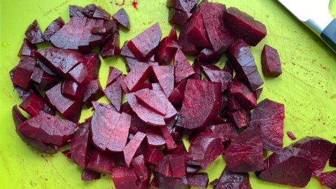 A cutting board with chopped beets and a knife to the top right.