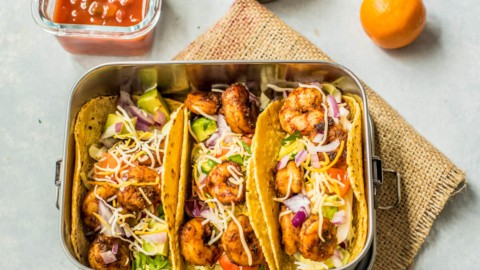 A stainless lunch container with shrimp tacos.