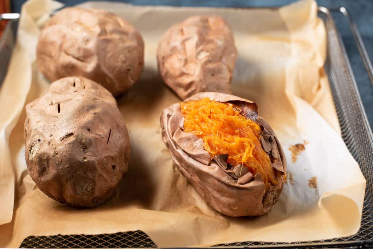 air fryer sweet potatoes on a parchment paper lined sheet from the air fryer with one cut open to expose the sweet potato.