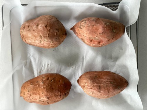 Four sweet potatoes on parchment paper before cooking in the air fryer.