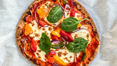 A veggie pizza made with naan bread and garnished with fresh basil.