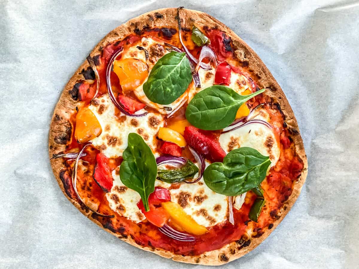 A veggie pizza that is garnished with basil and made with naan bread.