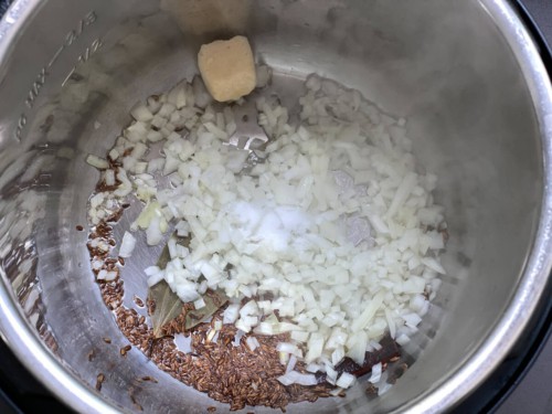 Instant pot with cumin seeds and onion.