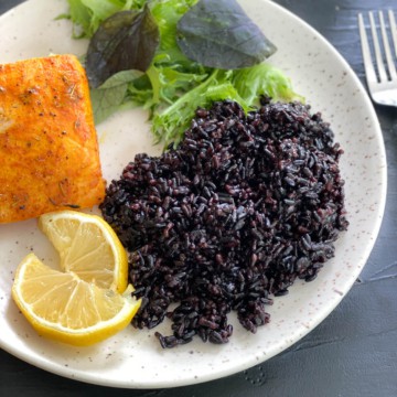A plate with black rice, lemon wedges, and salmon.