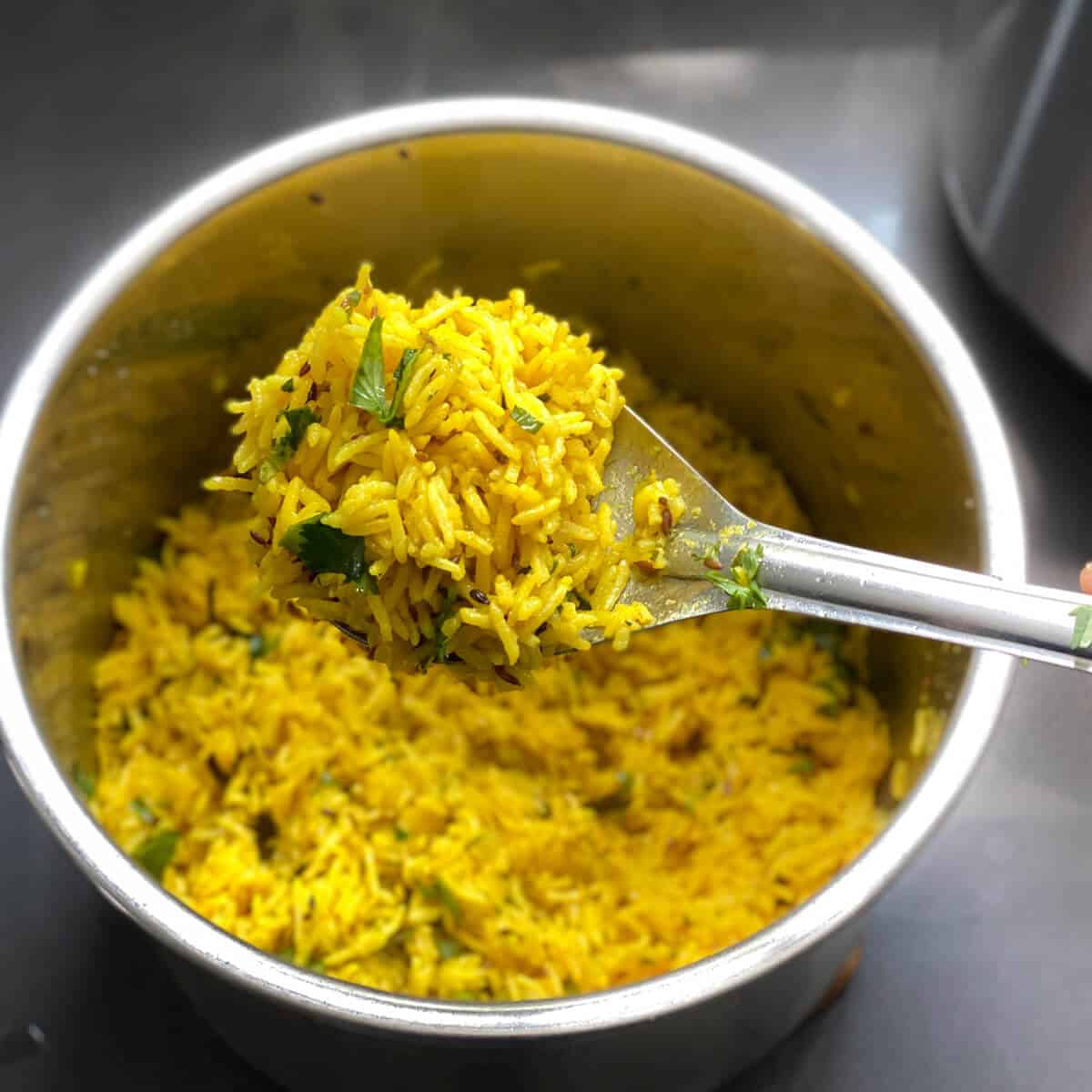 A silver spoon with yellow turmeric rice over the instant pot filled with turmeric rice.