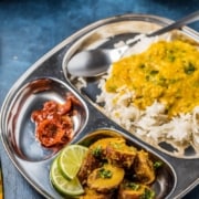 A silver tray on a blue counter with Bombay Aloo in the front corner and moong dal in the back of the tray with the words Instant Pot Bombay Potatoes at the top.