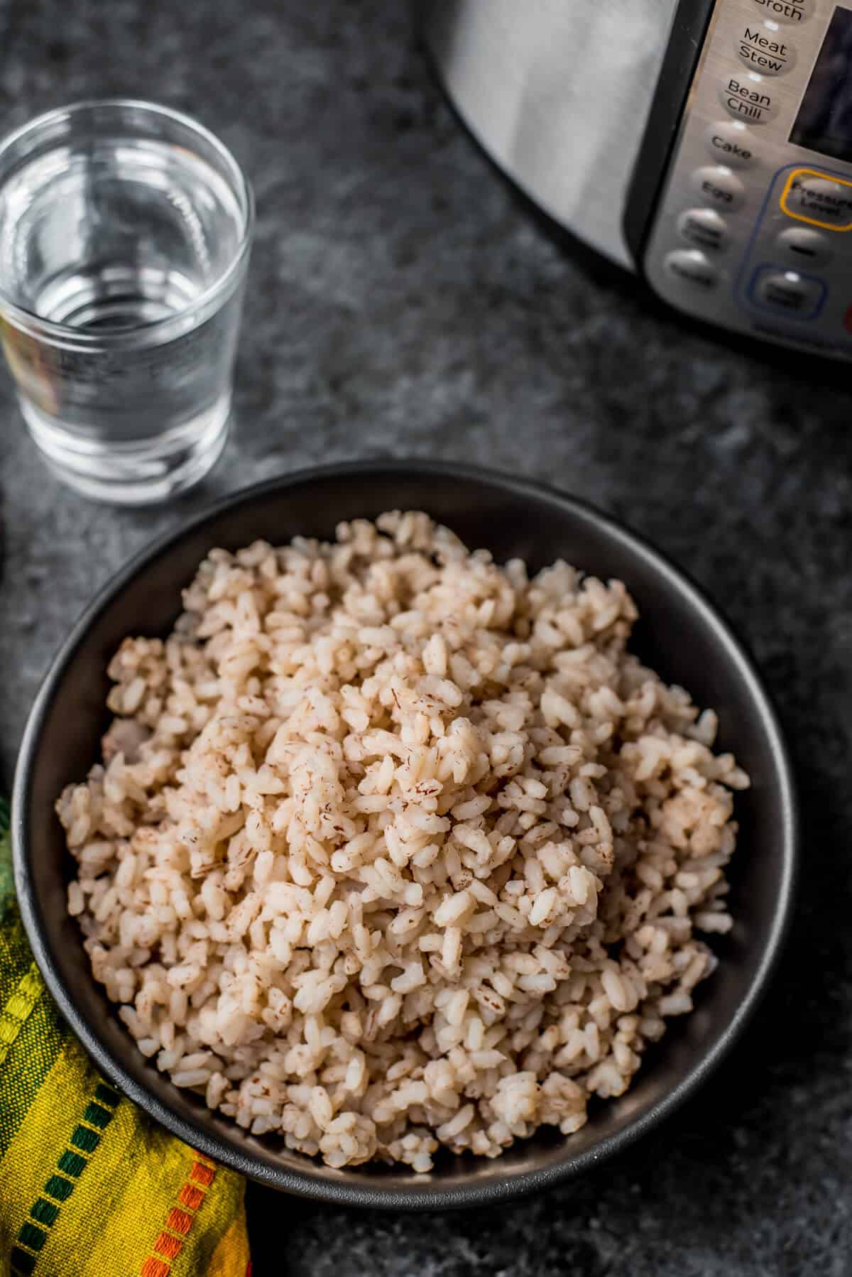A black bowl with kerala matta rice after cooking in the Instant Pot with a glass of water to the top left and the Instant Pot in the top right of the photo.