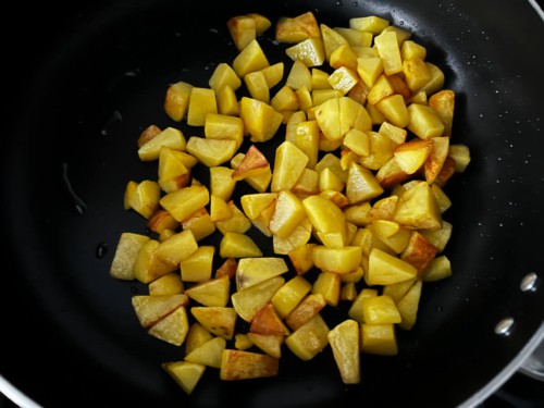 A wok with diced potatoes being shallow fried.