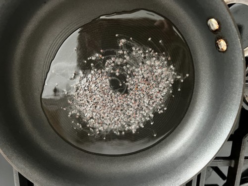 A non-stick skillet with oil and mustard seeds.