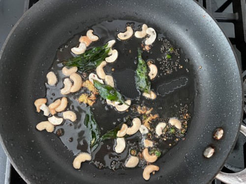 A non-stick skillet with chilies, cashews, and curry leaves.