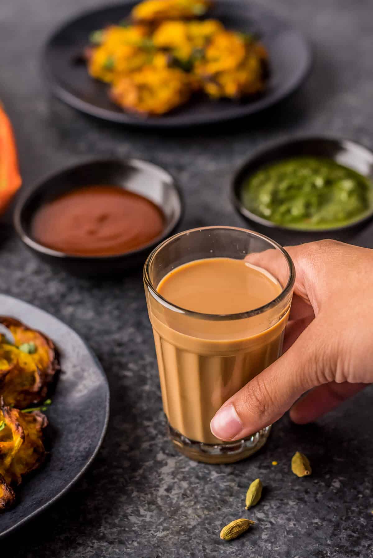 A hand grabbing a small glass of masala chai.