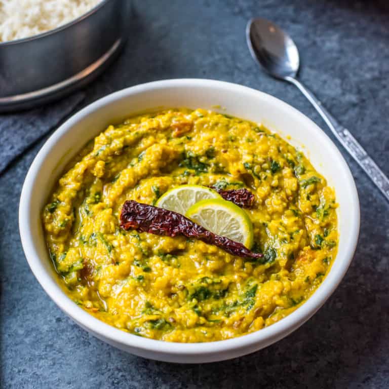 A white bowl with dal palak topped with lemons and a silver spoon in the back.