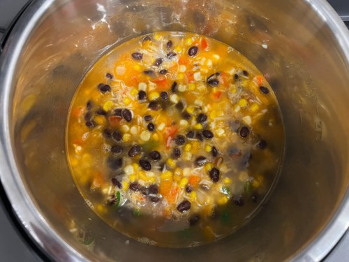 Adding liquid to a pot with corn, beans, and rice.