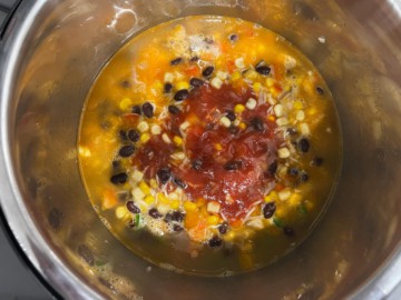 Adding tomatoes to an Instant Pot with broth, beans, rice, and vegetables.