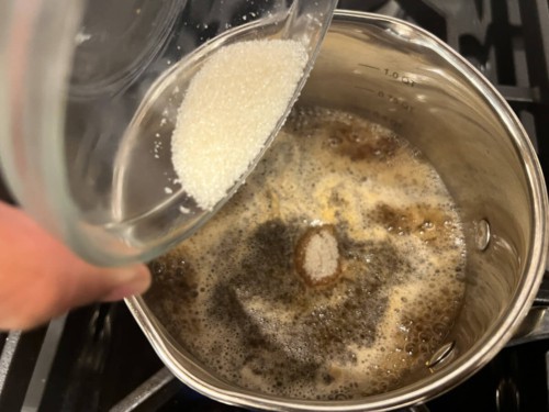 Adding tea leaves and sugar to boiling water.