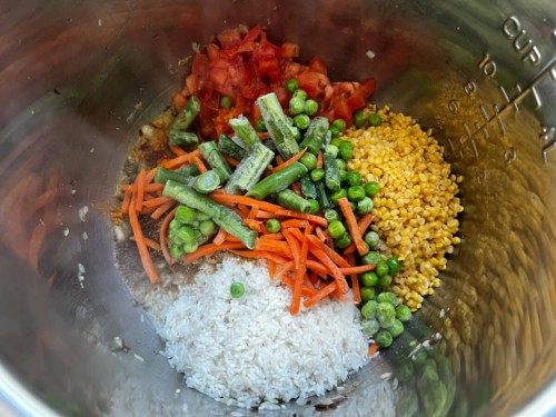 Vegetables, rice, spices and aromatics in the inner pot of an Instant Pot.
