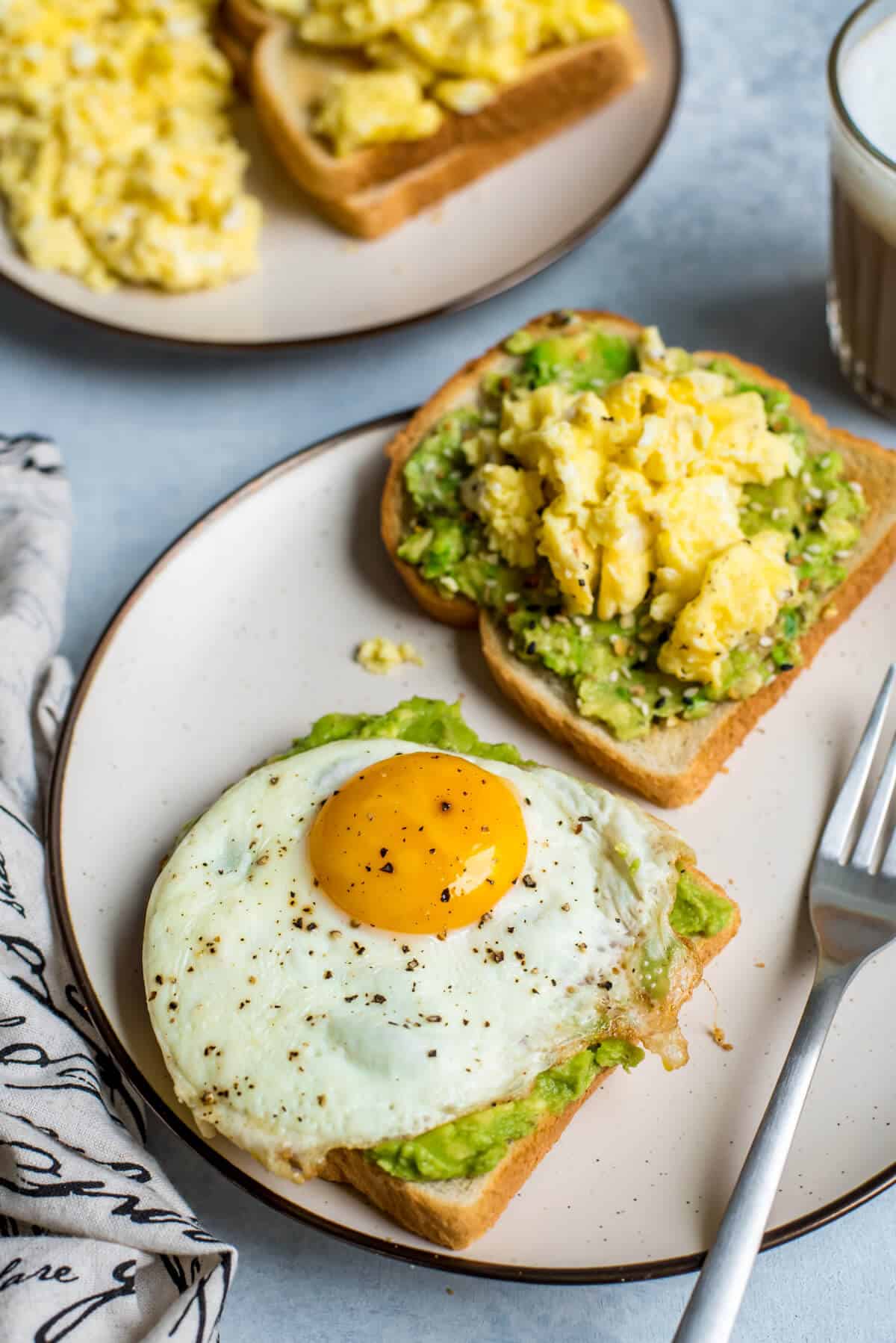 Two slices of toast topped with avocado and egg - one with a fried egg, another with scrambled eggs.