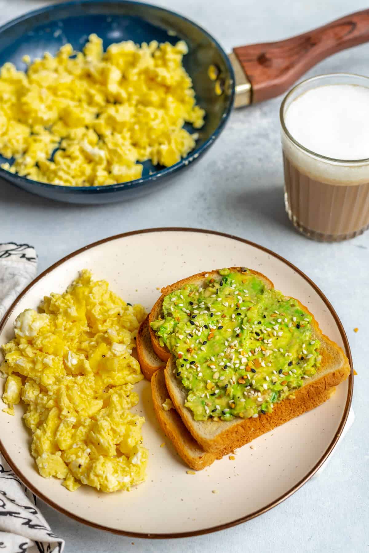 A plate with avocado toast and a side of scrambled eggs.