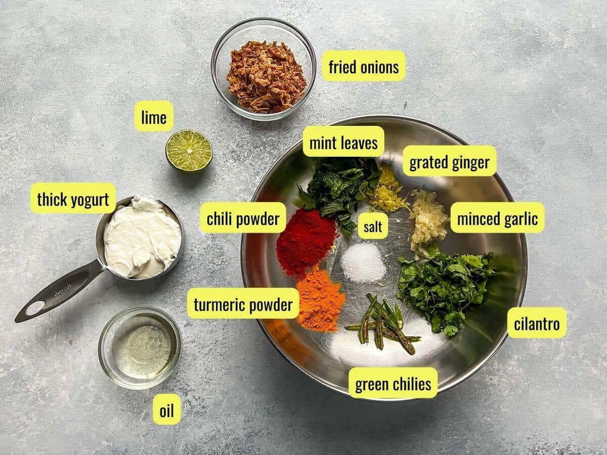 Ingredients for chicken biryani on a grey counter labeled with the different names of each ingredient.