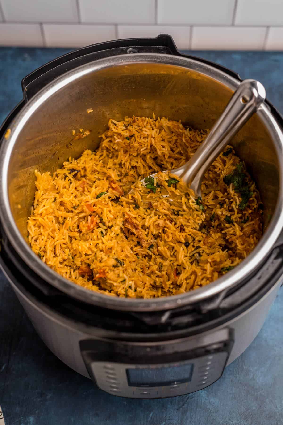 An instant pot with cooked chicken biryani and a silver spoon in the right corner of the Instant Pot.