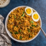 A white bowl filled with fresh Instant Pot Chicken Biryani topped with a cooked hard boiled egg in the right corner.