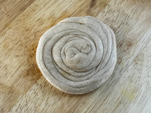 A flattened disk of lacha paratha dough on a wooden counter.