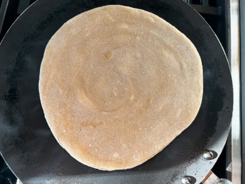 A non-stick skillet with a lacha paratha cooking on the first side.