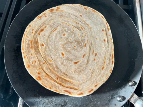 A non-stick skillet with lacha paratha after being flipped in the pan.