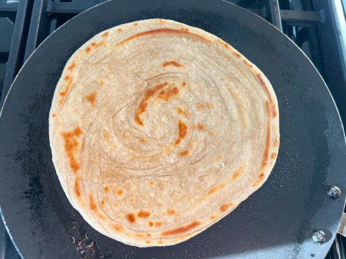 A non-stick skillet with lacha paratha cooked to a golden brown finish in the pan.