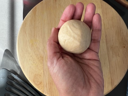 A hand holding a golf-ball sized amount of lacha paratha dough.