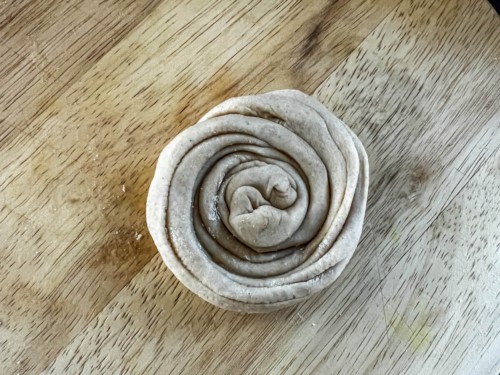 A tight coil of lacha paratha dough on a wooden counter.