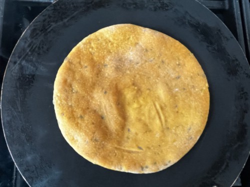A flipped paratha on a skillet brushed with ghee.