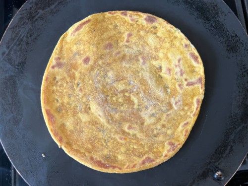 Flipped and ghee brushed masala paratha on a skillet.
