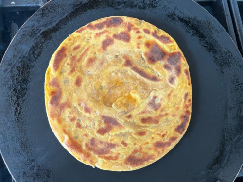 A cooked masala paratha on a skillet.