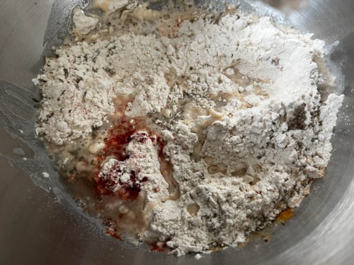 A silver mixing bowl with water being added to the dry ingredients.