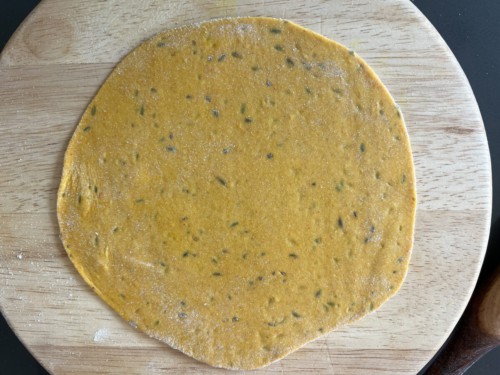 A round cutting board with a flattened masala paratha after rolling out.