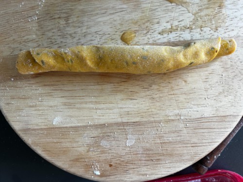 A round wooden cutting board with a rolled up log of masala paratha dough.