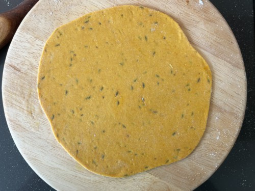 A round wooden counter with a rolled out masala roti dough disk.